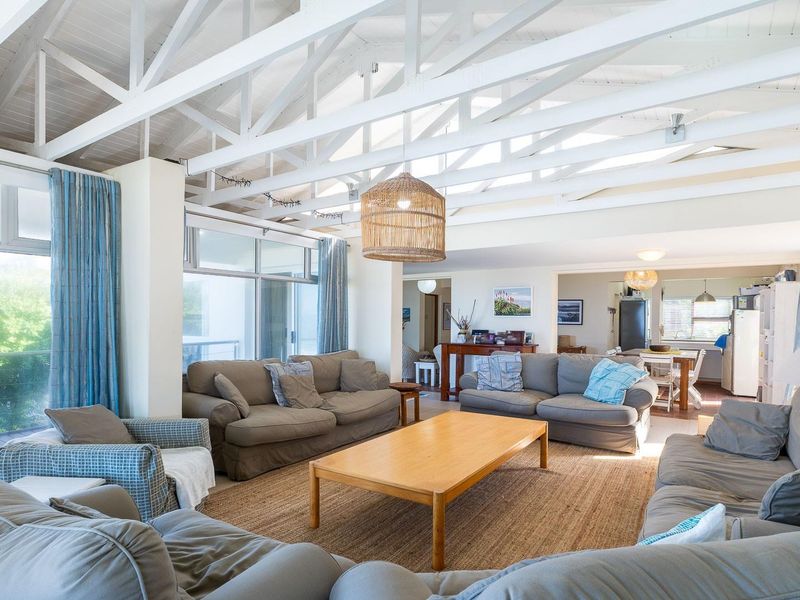 Spacious open-plan living area featuring a high vaulted ceiling with exposed white timber trusses, large windows, and sliding doors leading to an outdoor space.