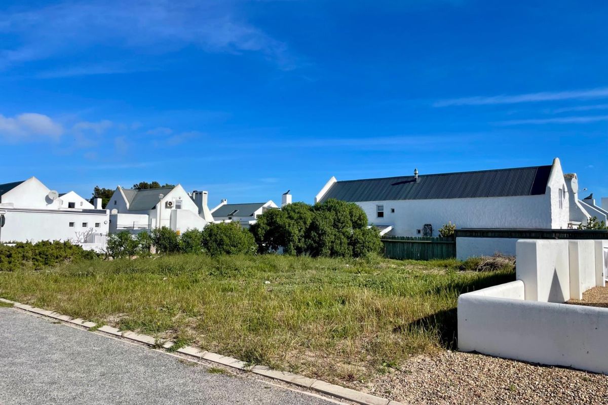 Street view showing the approach to the property with a paved road, gravel verge, and surrounding residential houses.