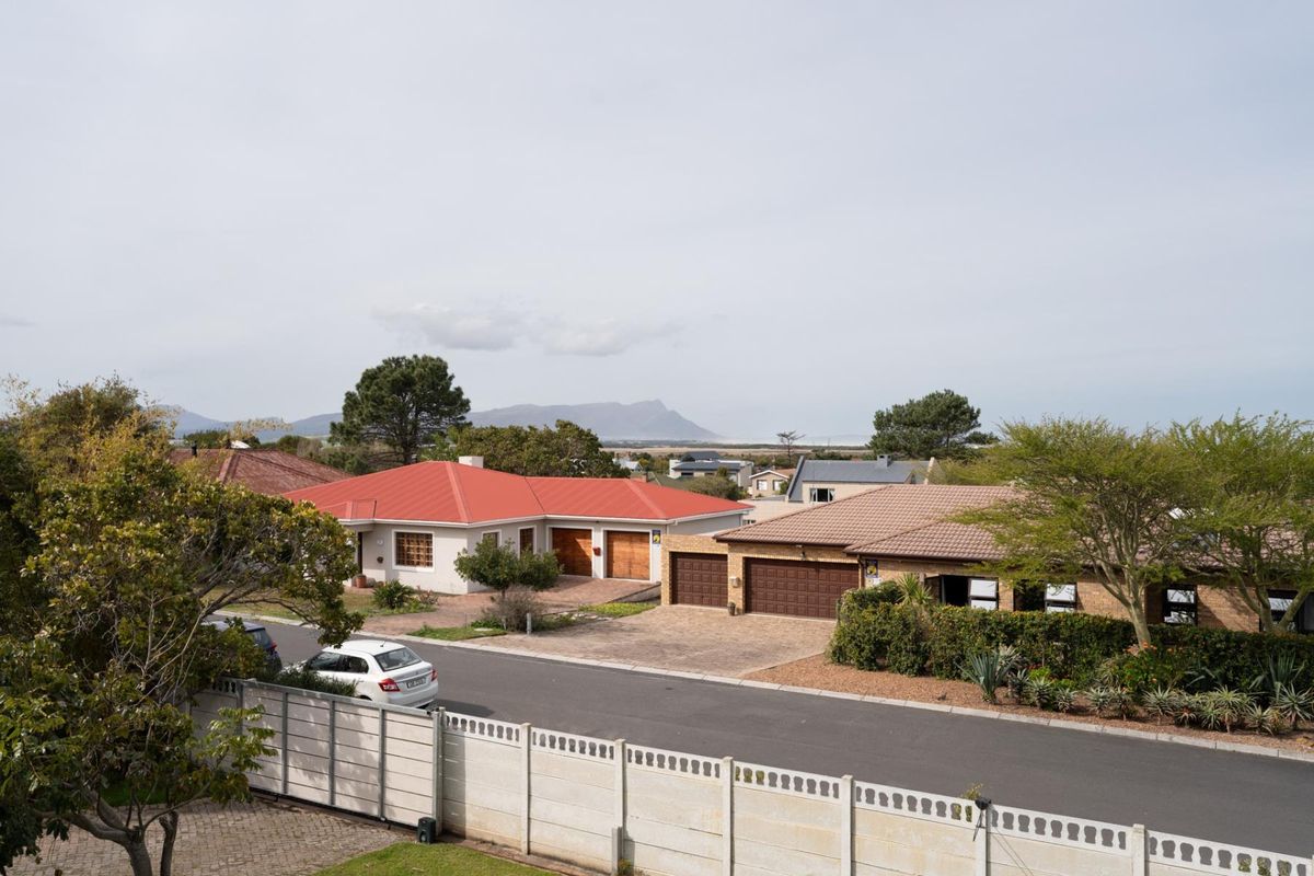 Aerial view of a residential street featuring houses with tiled and metal roofs, paved driveways, and secure perimeter walling in a suburban setting.