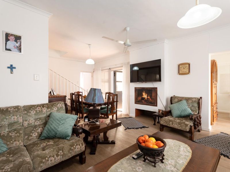 A comfortable living room featuring a built-in fireplace, ceiling fan, and an open-plan layout leading to a dining area and staircase.