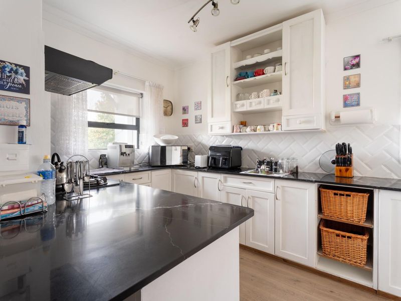 A well-maintained kitchen featuring white cabinetry, black stone countertops, a stylish herringbone backsplash, and modern track lighting.