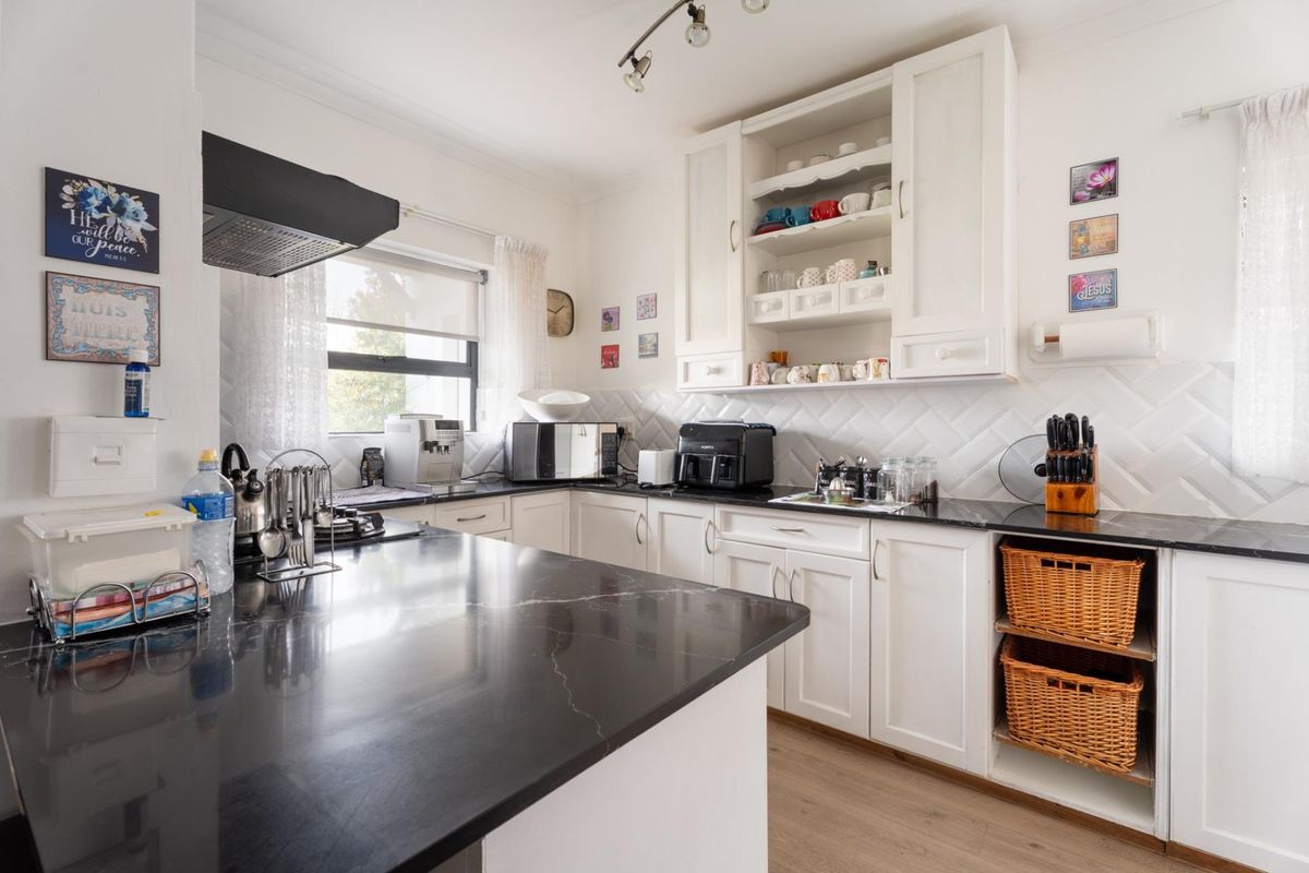 A well-maintained kitchen featuring white cabinetry, black stone countertops, a stylish herringbone backsplash, and modern track lighting.