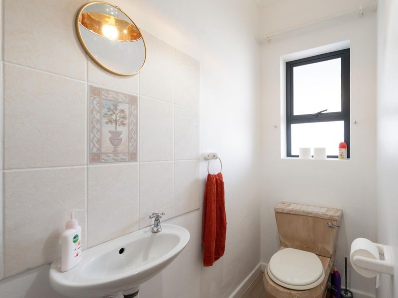 A compact bathroom featuring a wall-mounted basin, a toilet, and tiled splashback, providing essential functionality in a clean, well-lit space.