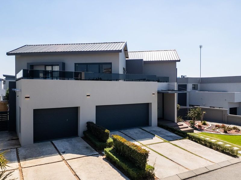 Modern double-story residence featuring a double garage, concrete driveway, and a spacious upper-level balcony with glass balustrades.