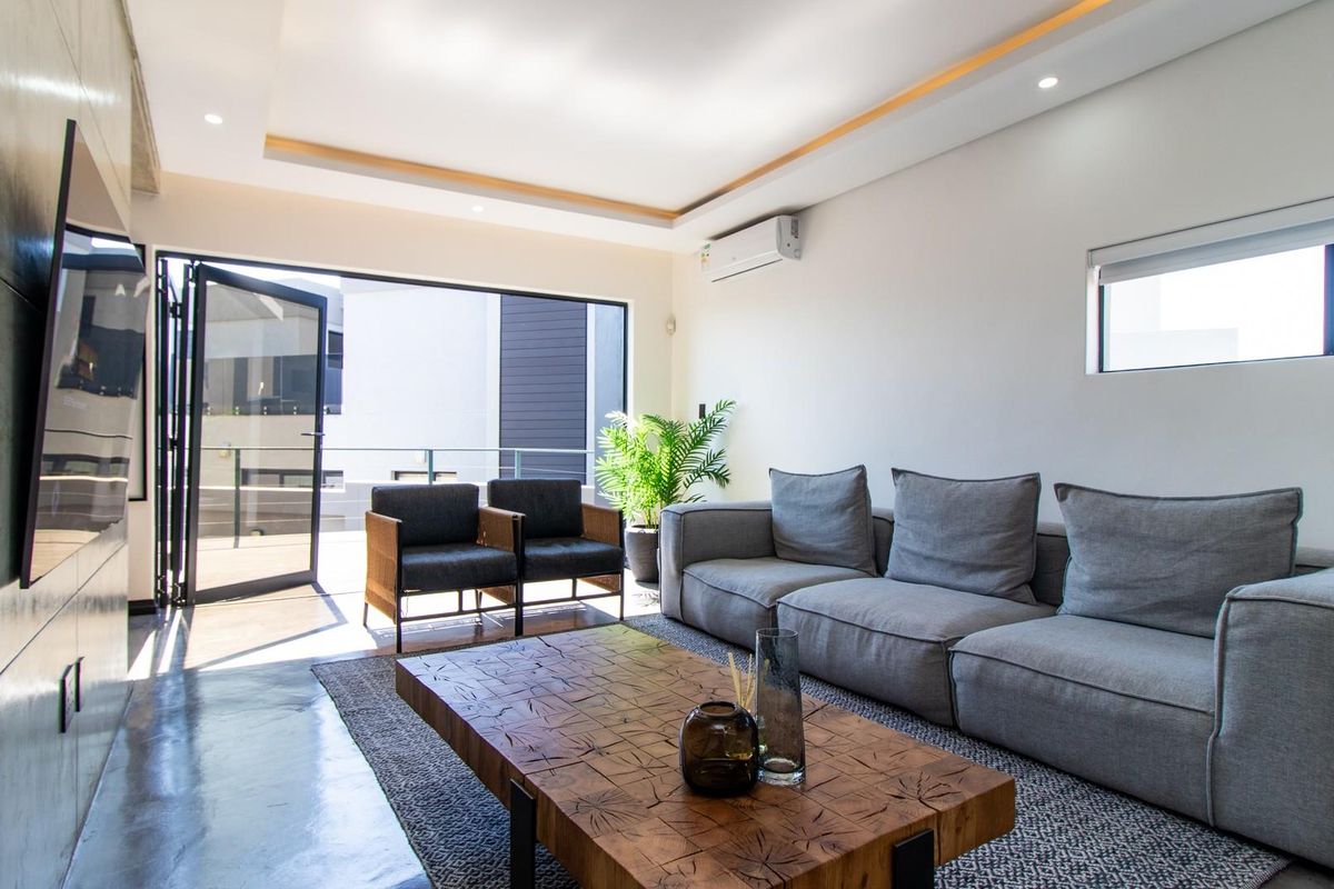 Modern living room featuring polished concrete floors, recessed ceiling lighting, and large bi-fold doors opening to an outdoor balcony area.