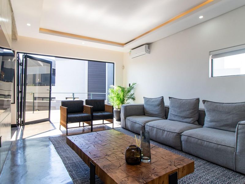 Modern living room featuring polished concrete floors, recessed ceiling lighting, and large bi-fold doors opening to an outdoor balcony area.