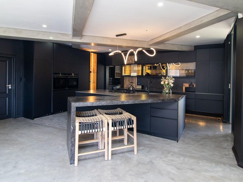 Modern, high-end kitchen featuring sleek black cabinetry, a large stone-topped island, polished concrete floors, and exposed structural beams with contemporary lighting.