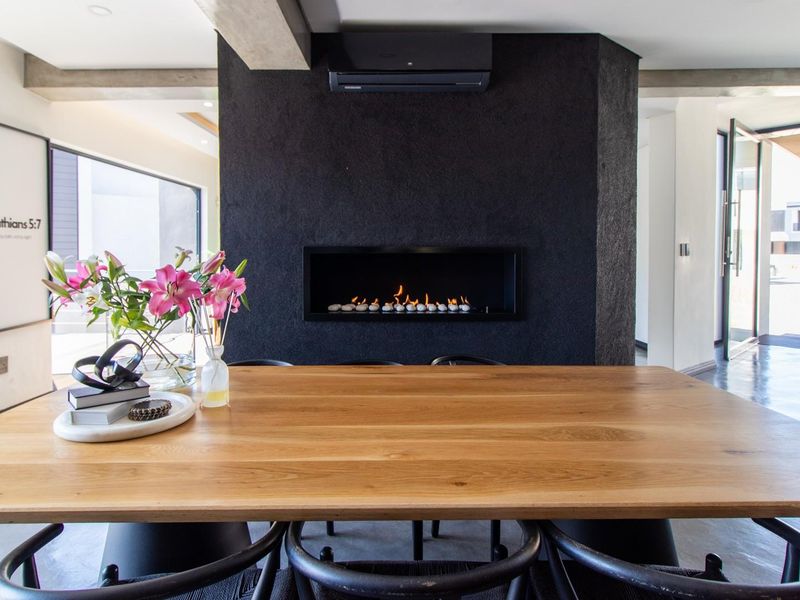 Modern dining area featuring a striking black feature wall with a built-in fireplace, polished concrete floors, and seamless access to outdoor spaces via bi-fold doors.