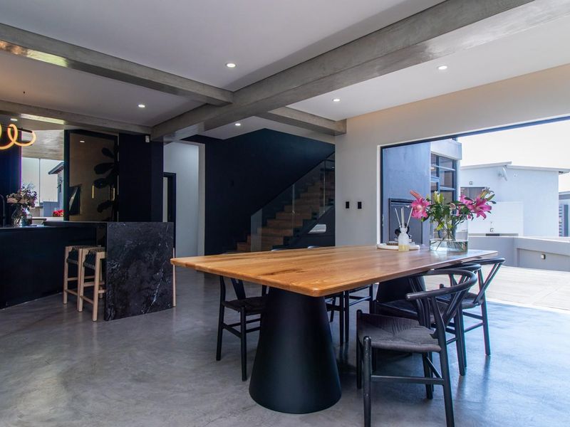 Modern open-plan living and dining area featuring polished concrete floors, exposed structural beams, a sleek kitchen with marble island, and seamless indoor-outdoor flow.