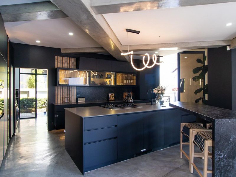 Modern, high-end kitchen featuring a large central island, sleek matte cabinetry, integrated appliances, and striking exposed concrete beams with polished concrete floors.
