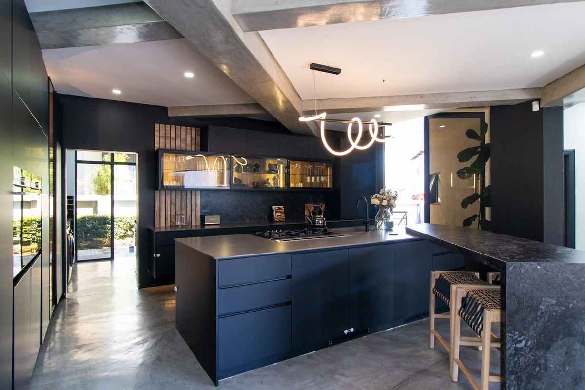 Modern, high-end kitchen featuring a large central island, sleek matte cabinetry, integrated appliances, and striking exposed concrete beams with polished concrete floors.