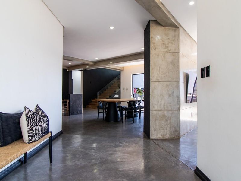 Modern open-plan living area featuring polished concrete floors, architectural exposed concrete columns, and a seamless flow towards the dining space and staircase.
