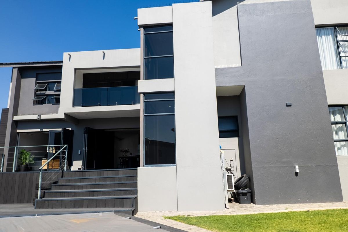 Modern rear elevation featuring a multi-level design with a spacious deck, glass balustrades, and large aluminium-framed windows and doors.