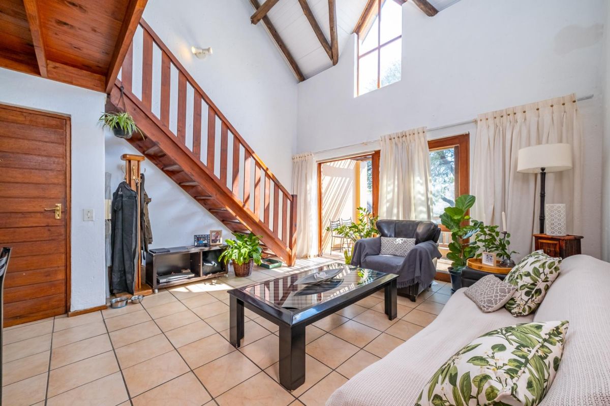 Spacious living room featuring high vaulted ceilings with exposed timber beams, tiled flooring, and a wooden staircase leading to an upper level.
