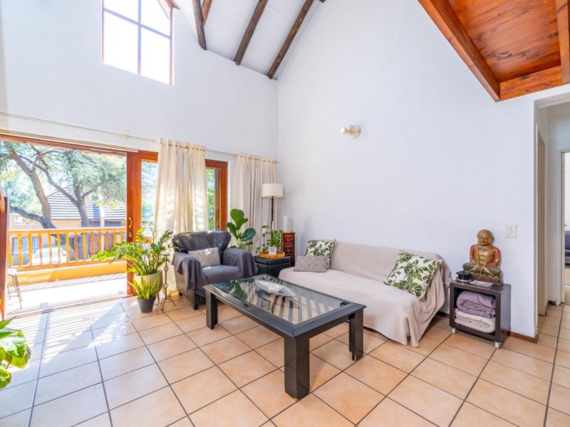 Spacious living room featuring a high vaulted ceiling with exposed timber beams, tiled flooring, and large sliding doors opening onto a private balcony.