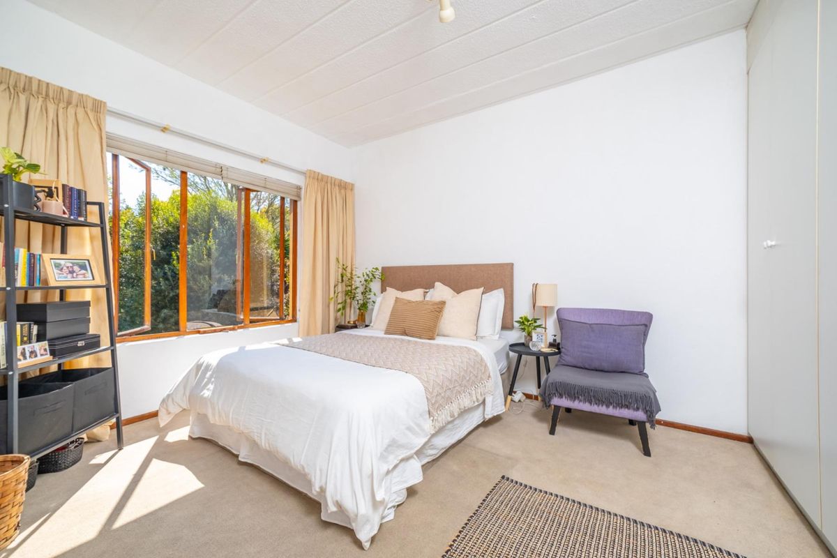 A bright bedroom featuring a large window, neutral carpet flooring, and a built-in wardrobe, offering a comfortable and functional living space.
