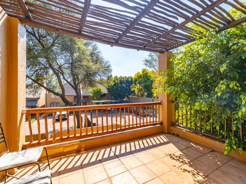 A covered balcony featuring a rustic wooden pergola, tiled flooring, and a wooden balustrade overlooking the complex grounds.