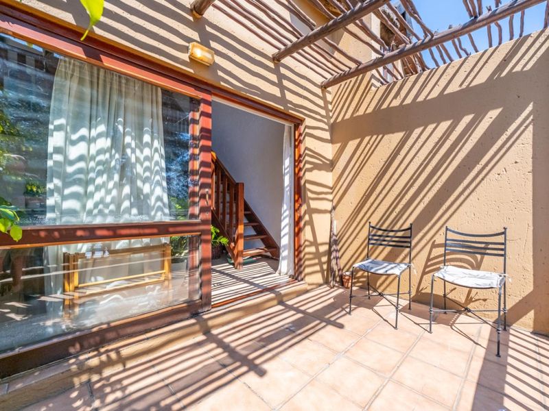 A sunlit patio featuring tiled flooring, a wooden pergola structure, and a sliding glass door providing access to the interior staircase.