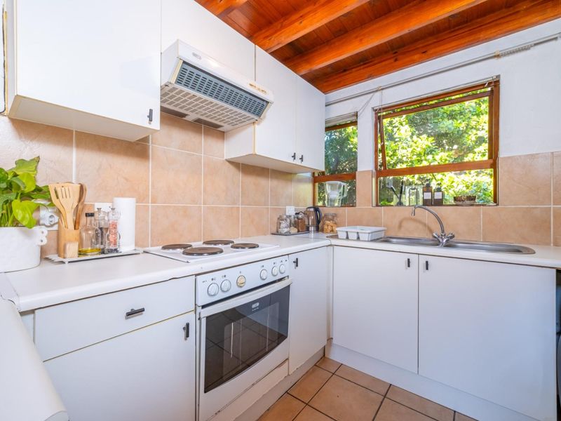 Compact kitchen featuring white cabinetry, electric stove, oven, extractor fan, tiled backsplash, and exposed timber ceiling beams with natural light.