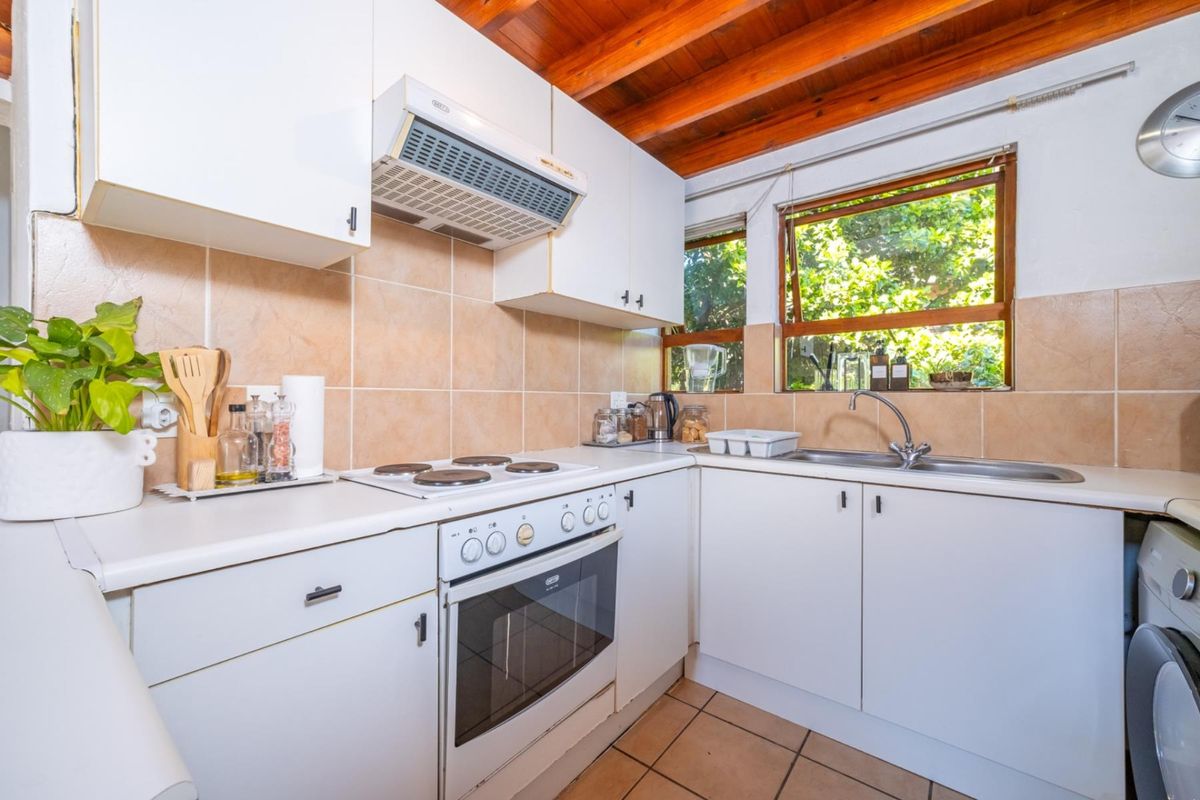 Compact kitchen featuring white cabinetry, electric stove, oven, extractor fan, tiled backsplash, and exposed timber ceiling beams with natural light.