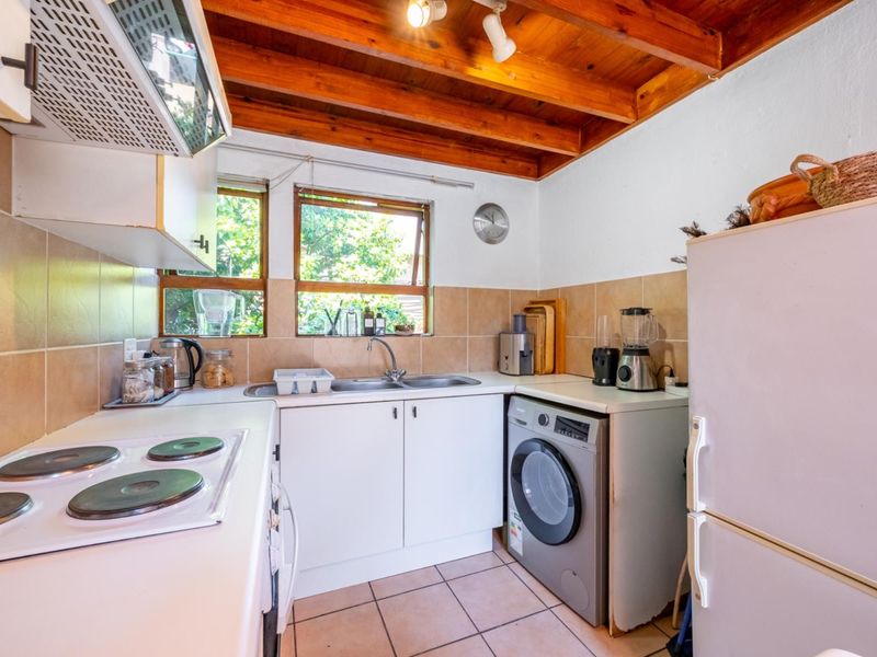Compact kitchen featuring white cabinetry, electric hob, extractor fan, double sink, tiled splashback, and exposed timber ceiling beams.