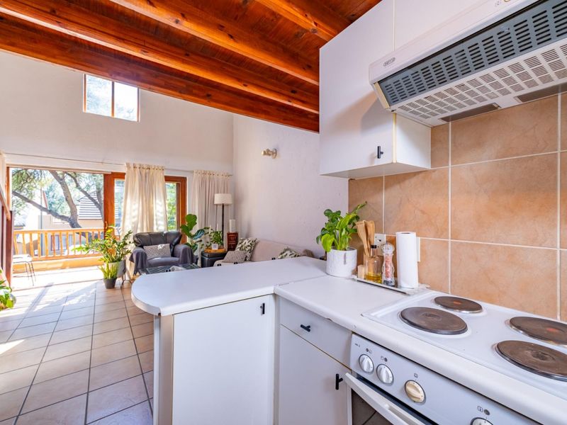 Open-plan living area featuring exposed timber beams, tiled floors, and a functional kitchen with built-in cabinetry, leading to an outdoor balcony.