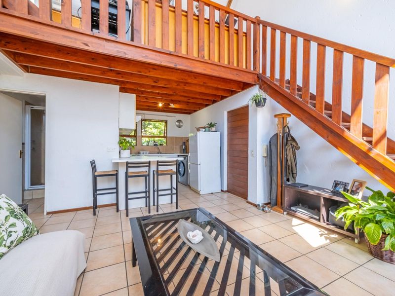 Open-plan living area featuring a kitchen with breakfast bar, tiled flooring, and a prominent wooden staircase leading to a mezzanine level.
