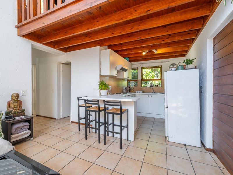 Open plan kitchen area featuring tiled floors, white cabinetry, a breakfast bar, and exposed timber ceiling beams with a mezzanine level above.