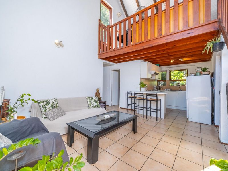 Open-plan living area featuring tiled floors, a kitchen with built-in cabinetry, and a wooden mezzanine loft level with a balustrade.