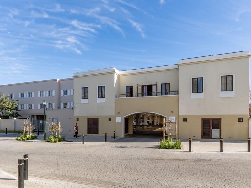 Front elevation of the apartment complex featuring a paved driveway, secure gated entrance, and upper-level balcony.