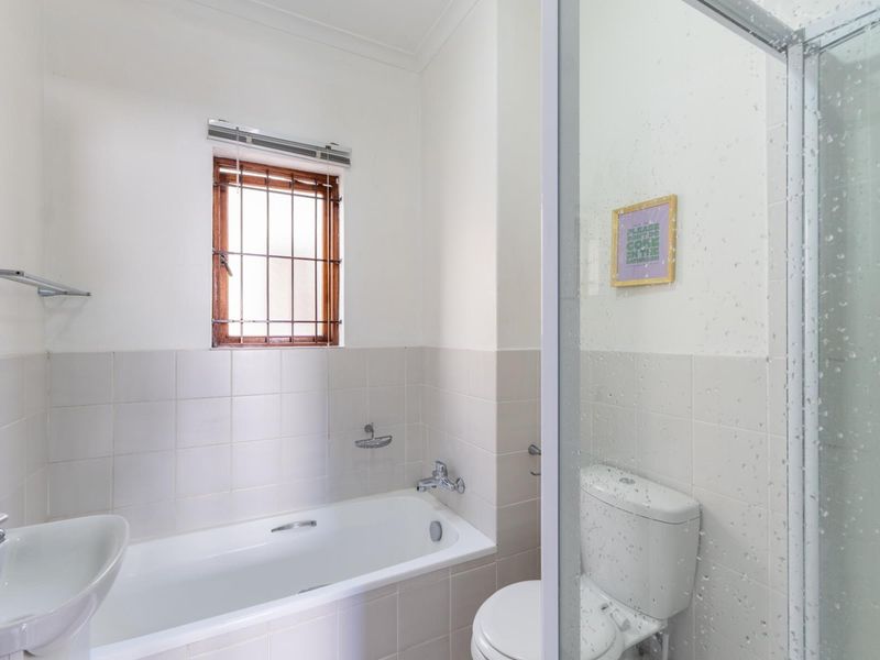 A functional bathroom featuring a bathtub, separate shower enclosure, toilet, and washbasin with neutral wall tiling.