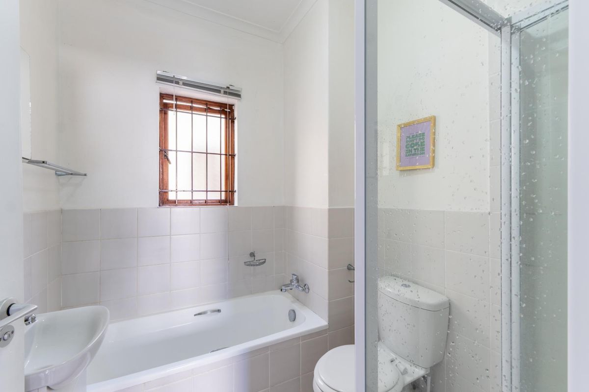 A functional bathroom featuring a bathtub, separate shower enclosure, toilet, and washbasin with neutral wall tiling.