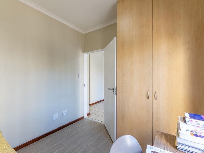 A bedroom featuring light-toned laminate flooring, neutral walls, and a large built-in wooden wardrobe, with an open doorway leading to an adjacent tiled area.