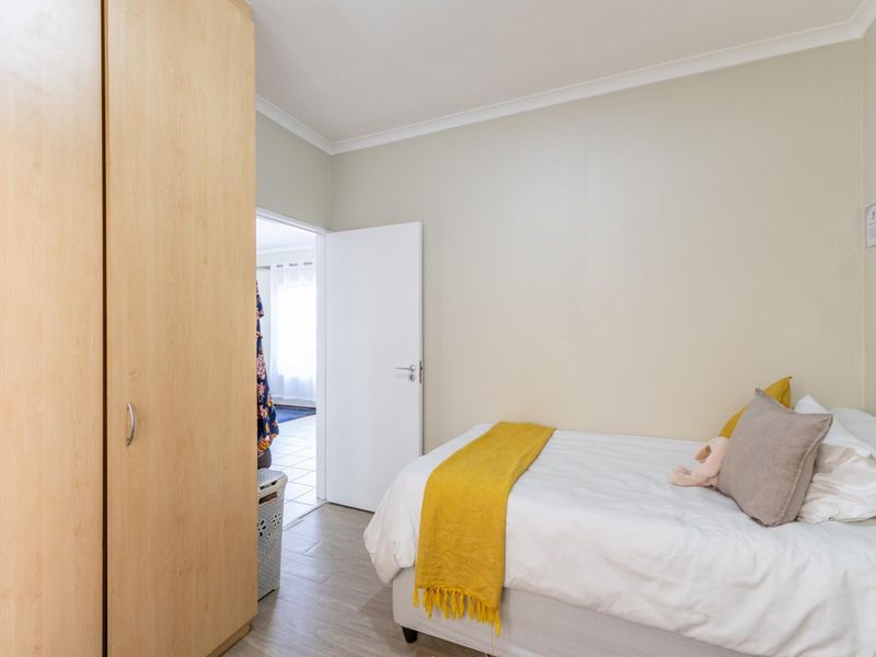 A well-maintained bedroom featuring light-toned tiled flooring, a built-in wardrobe, and neutral wall finishes.