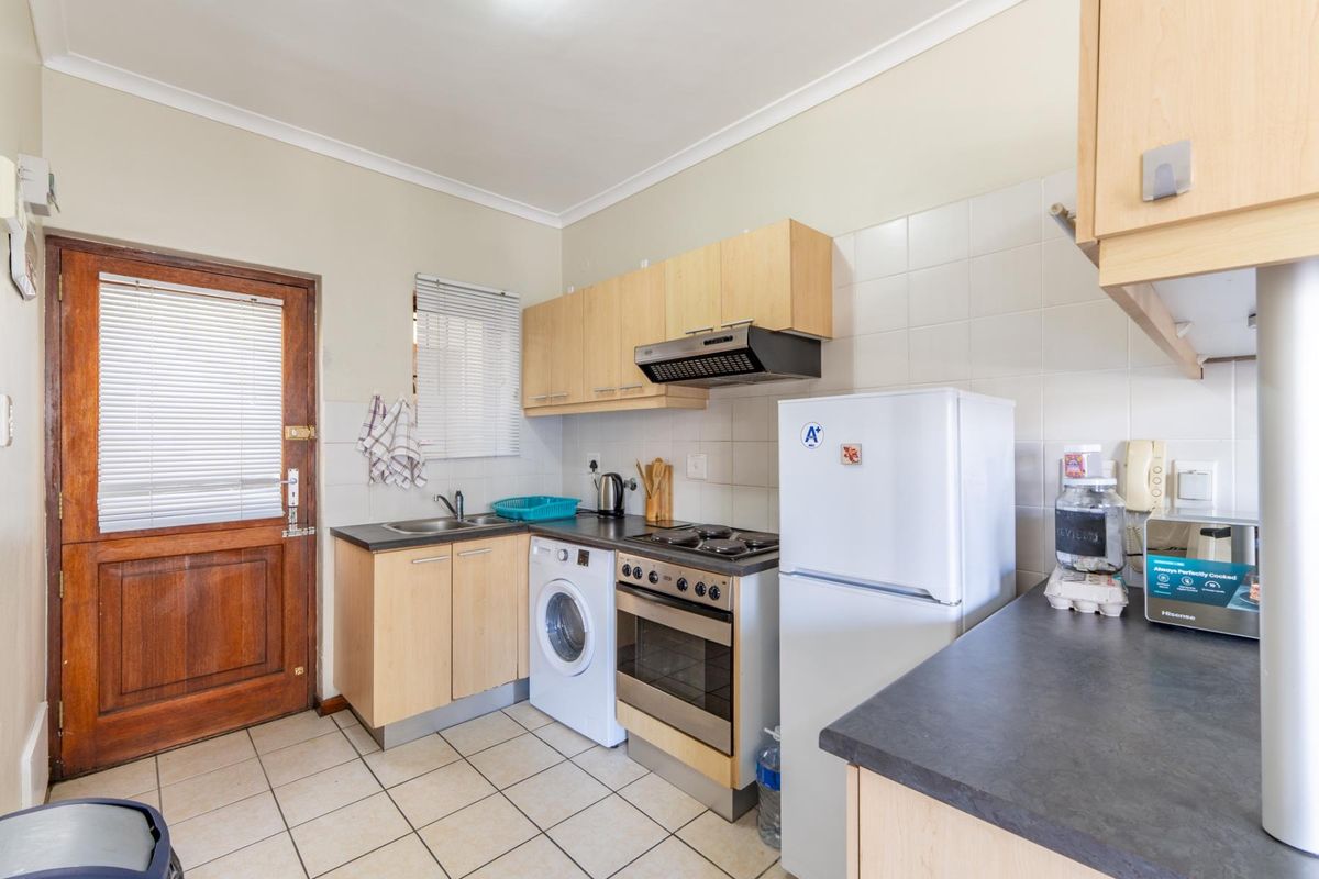 Functional kitchen featuring laminate cabinetry, built-in oven with hob, extractor fan, stainless steel sink, and tiled flooring with direct exterior access.