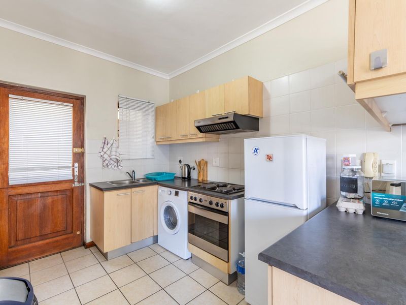 Functional kitchen featuring laminate cabinetry, built-in oven with hob, extractor fan, stainless steel sink, and tiled flooring with direct exterior access.