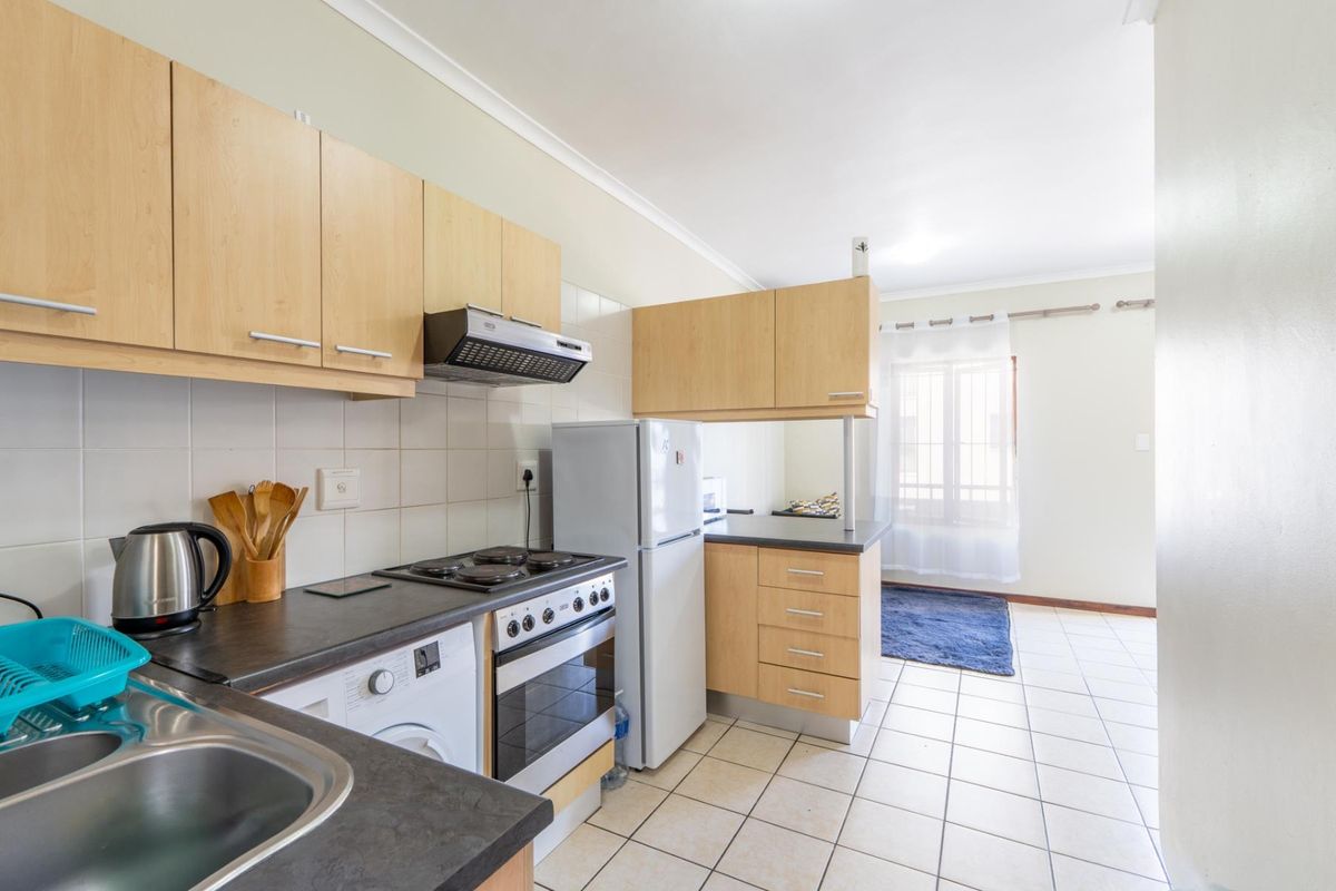 Functional kitchen featuring light wood-finish cabinetry, dark laminate countertops, tiled backsplash, and integrated electric stove with extractor fan.