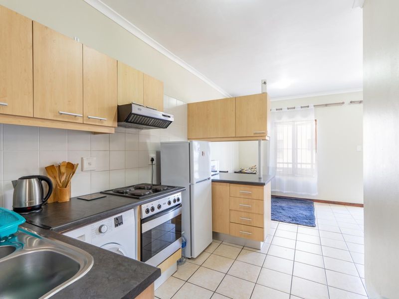 Functional kitchen featuring light wood-finish cabinetry, dark laminate countertops, tiled backsplash, and integrated electric stove with extractor fan.
