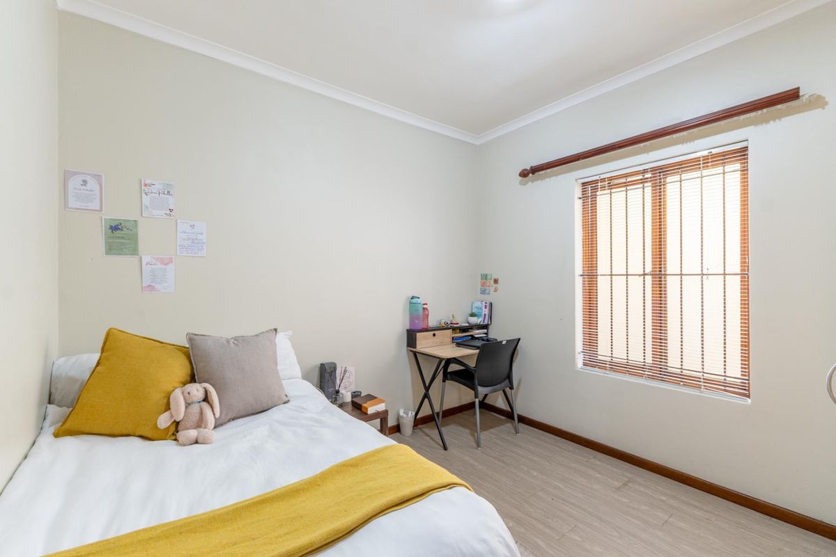 A well-lit bedroom featuring light-toned laminate flooring, neutral walls, and a window fitted with venetian blinds and a curtain rod.