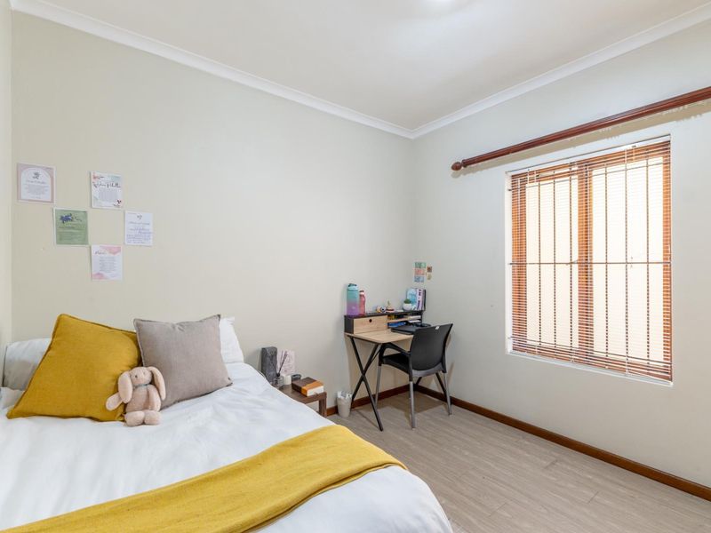A well-lit bedroom featuring light-toned laminate flooring, neutral walls, and a window fitted with venetian blinds and a curtain rod.