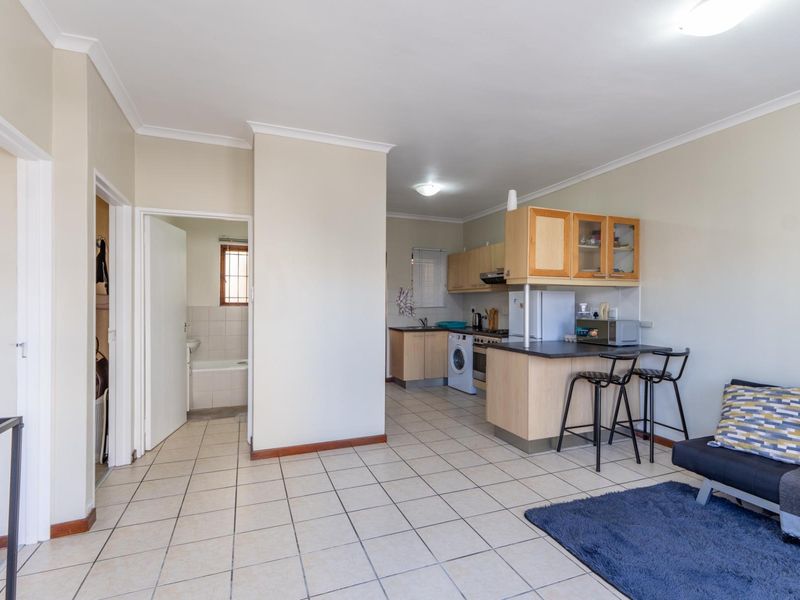 Open-plan living area featuring tiled flooring and a functional kitchen with built-in cabinetry, leading to an adjacent bathroom.
