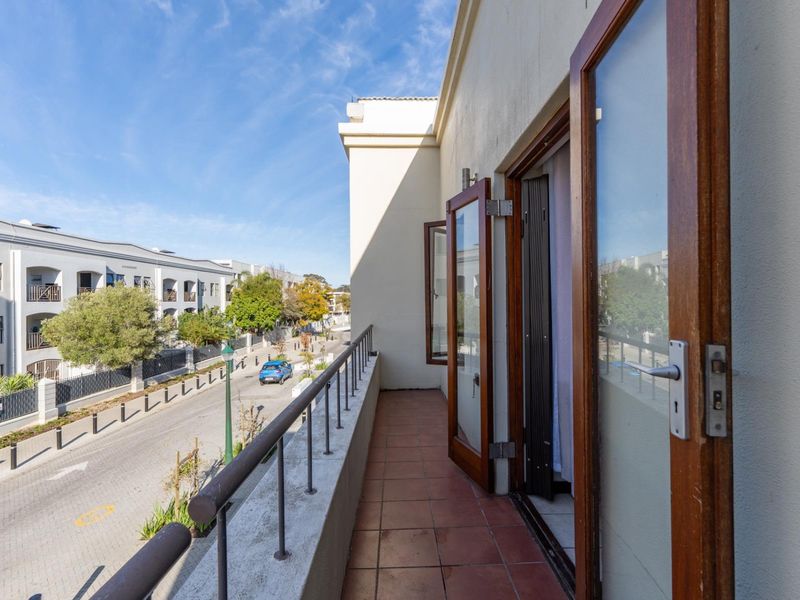A balcony featuring terracotta tiling and a metal balustrade, accessible via wooden framed double doors, overlooking the street.