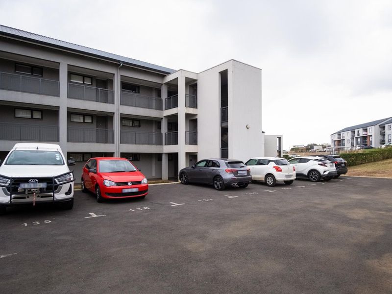 Exterior view of a multi-story apartment building featuring a paved parking area and balcony access for each unit.