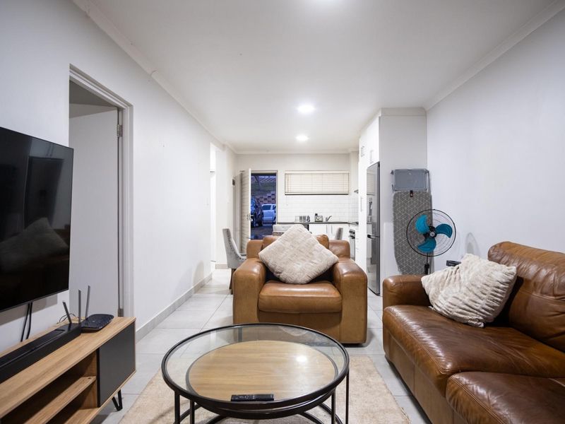 An open-plan living area featuring tiled flooring and recessed lighting, seamlessly connecting to a functional kitchen space with modern cabinetry and a subway tile backsplash.