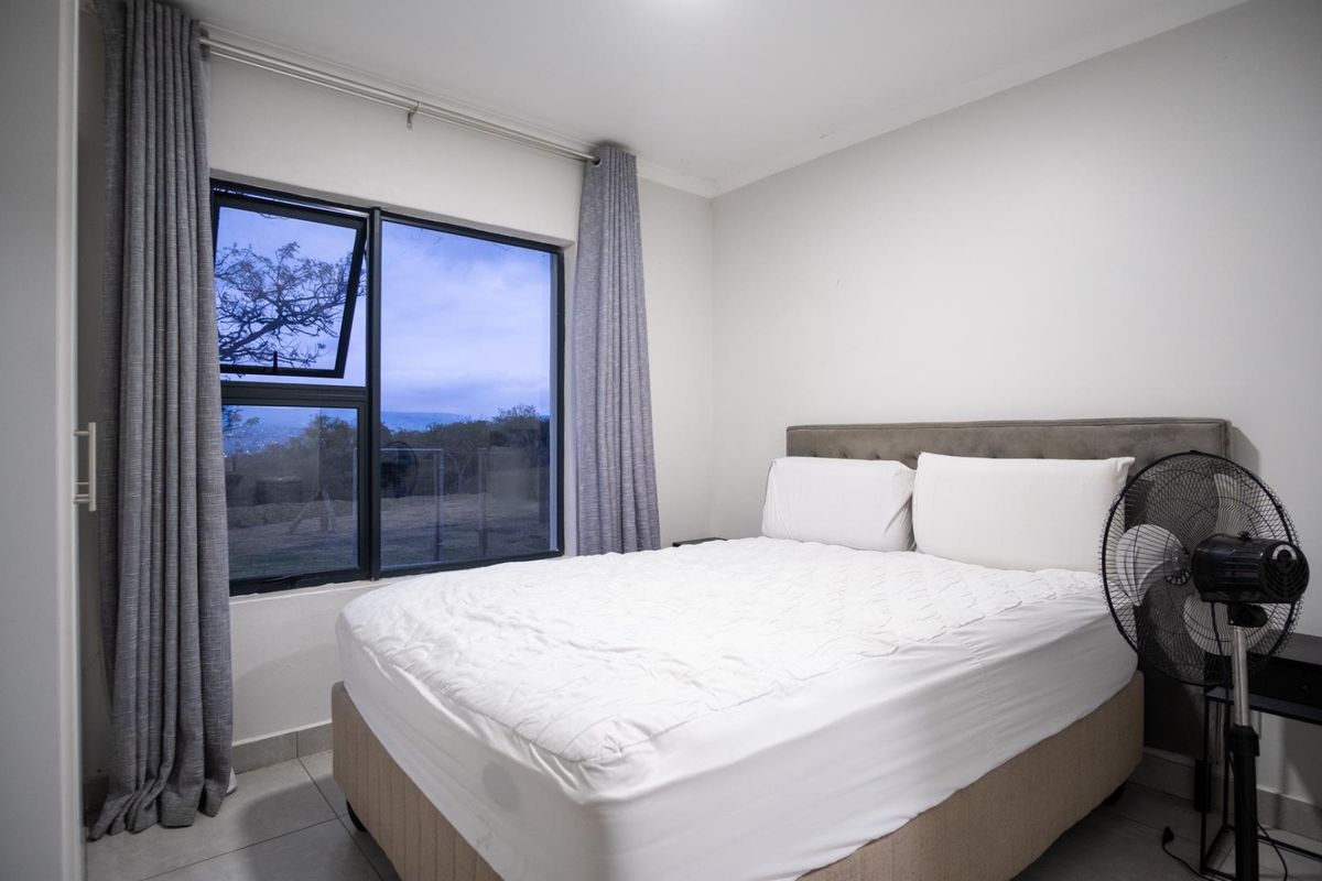 A well-maintained bedroom featuring tiled flooring and a large aluminium-framed window with views of the surrounding landscape.