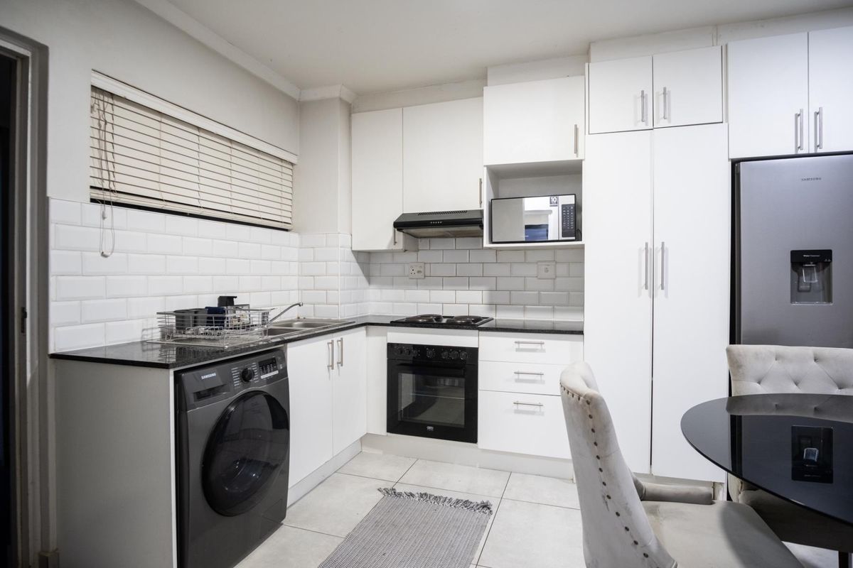 Modern kitchen featuring white cabinetry, granite countertops, subway tile backsplash, and integrated appliances including an oven, hob, and extractor fan.