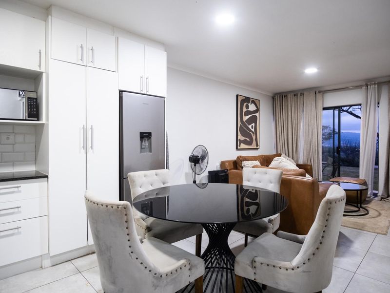 Open-plan living and dining area featuring modern white cabinetry, subway tile backsplash, tiled flooring, and sliding glass doors leading to an outdoor space.