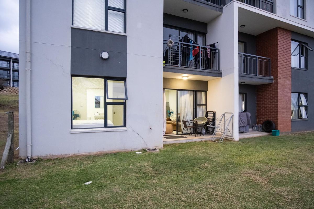Rear view of an apartment building featuring ground floor access, sliding glass doors, and balcony areas with visible exterior wall cracking.