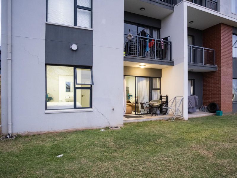 Rear view of an apartment building featuring ground floor access, sliding glass doors, and balcony areas with visible exterior wall cracking.