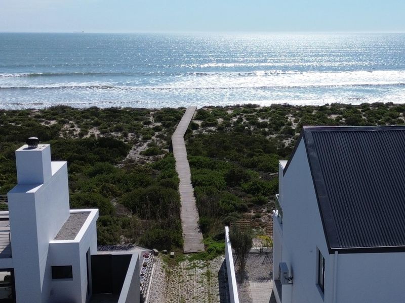 Aerial view of a coastal property featuring a private boardwalk leading directly to the beach, flanked by modern residential structures.